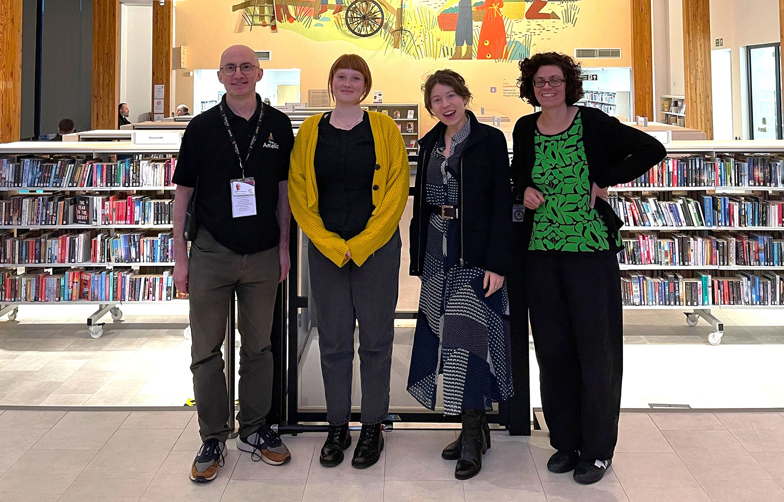 4 people posing for a photo in front of shelves of library books